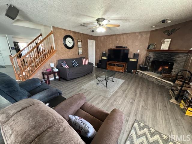 living room featuring ceiling fan, a stone fireplace, hardwood / wood-style floors, and a textured ceiling