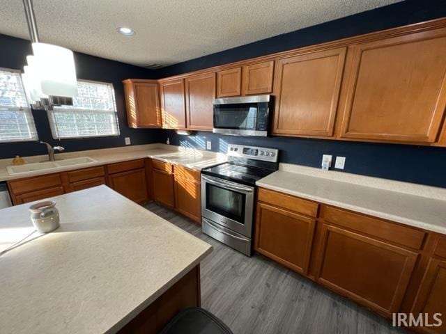 kitchen with sink, appliances with stainless steel finishes, hardwood / wood-style floors, hanging light fixtures, and a textured ceiling