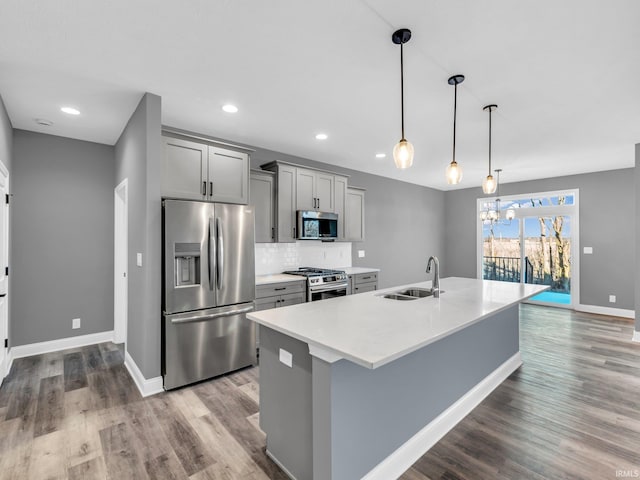 kitchen featuring sink, hanging light fixtures, gray cabinets, an island with sink, and stainless steel appliances