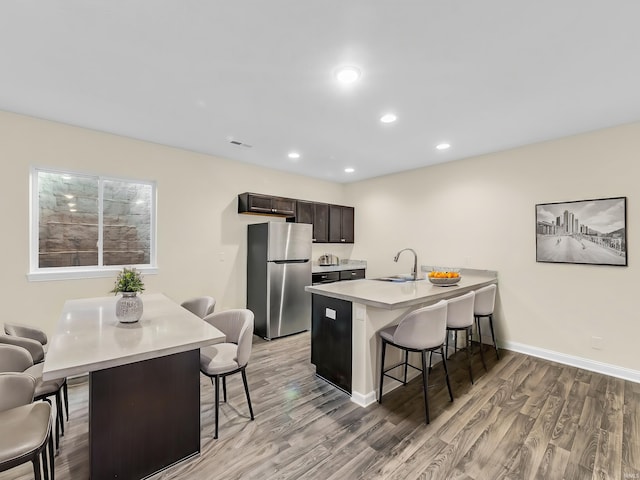 kitchen with dark brown cabinets, stainless steel fridge, a kitchen island with sink, and a breakfast bar area