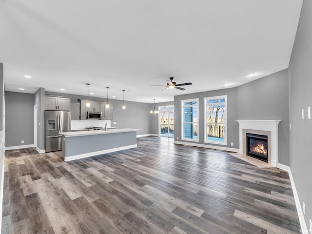 unfurnished living room featuring dark hardwood / wood-style flooring, sink, ceiling fan with notable chandelier, and a high end fireplace