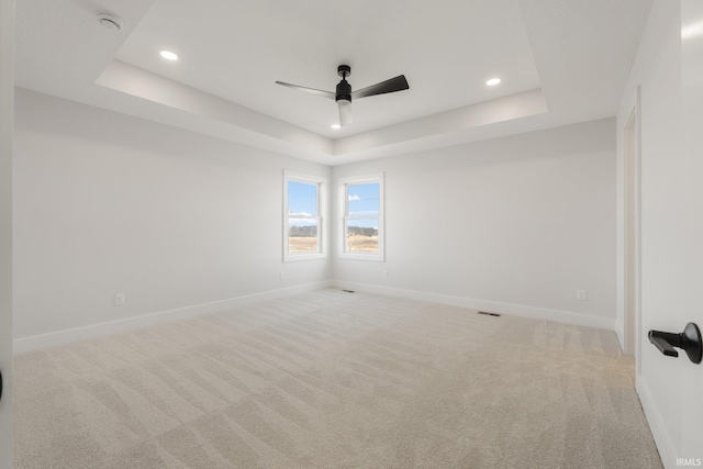 spare room with light colored carpet, a raised ceiling, and ceiling fan