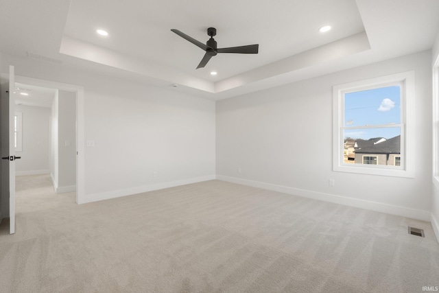 spare room featuring ceiling fan, light colored carpet, and a tray ceiling