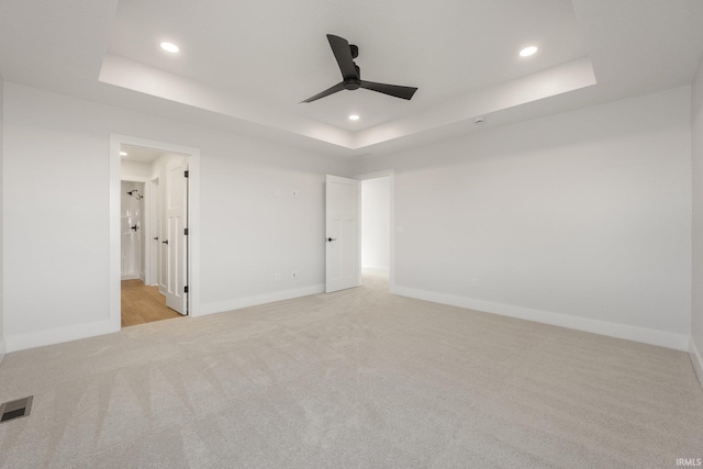 carpeted spare room featuring ceiling fan and a raised ceiling