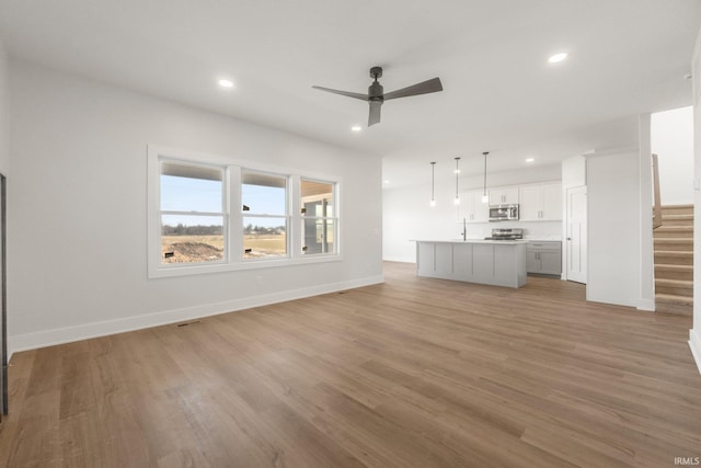 unfurnished living room featuring sink, light hardwood / wood-style floors, and ceiling fan