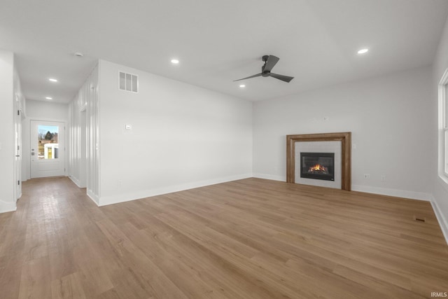 unfurnished living room with ceiling fan, a tiled fireplace, and light hardwood / wood-style flooring