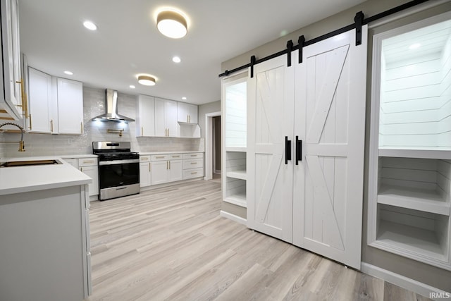 kitchen featuring wall chimney exhaust hood, sink, white cabinetry, stainless steel stove, and a barn door