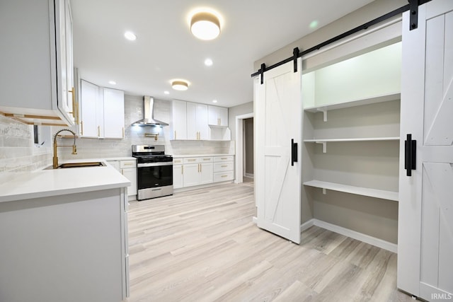 kitchen with sink, white cabinetry, stainless steel range, a barn door, and wall chimney range hood