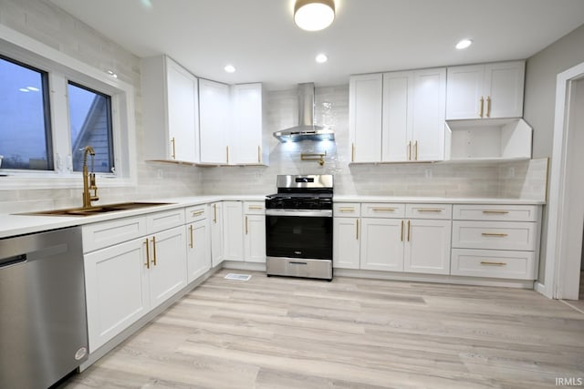 kitchen with wall chimney range hood, sink, white cabinets, and appliances with stainless steel finishes