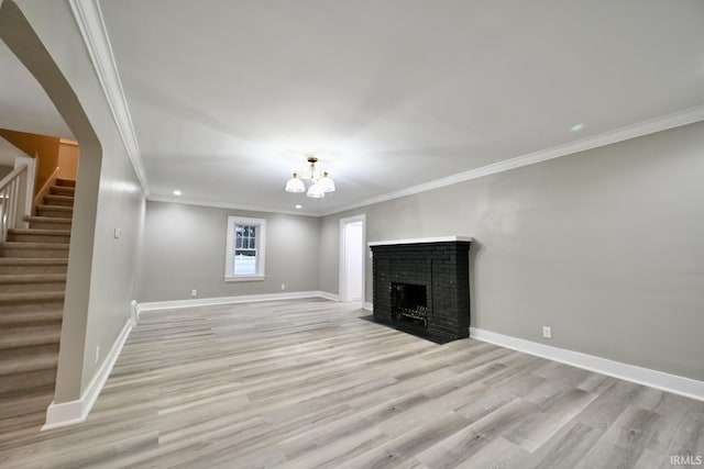 unfurnished living room featuring an inviting chandelier, a brick fireplace, crown molding, and light hardwood / wood-style flooring