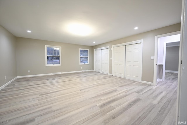 unfurnished bedroom with two closets and light wood-type flooring