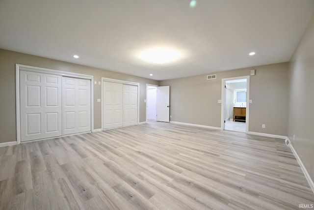 unfurnished bedroom featuring multiple closets, ensuite bath, and light hardwood / wood-style flooring