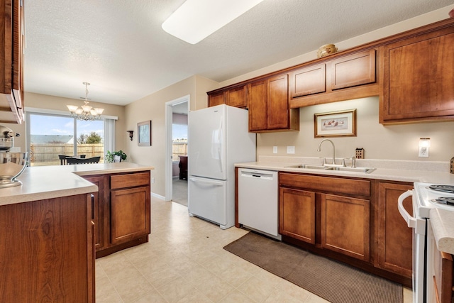 kitchen featuring sink, hanging light fixtures, white appliances, a textured ceiling, and an inviting chandelier