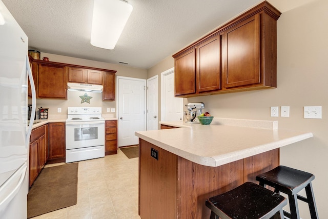 kitchen featuring white appliances, a breakfast bar area, kitchen peninsula, and a textured ceiling