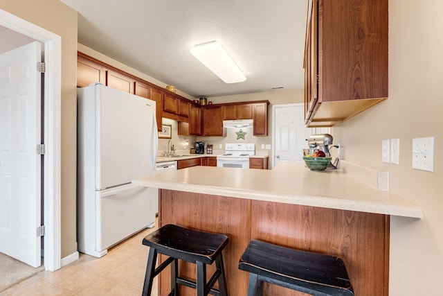 kitchen with a breakfast bar, sink, a textured ceiling, kitchen peninsula, and white appliances