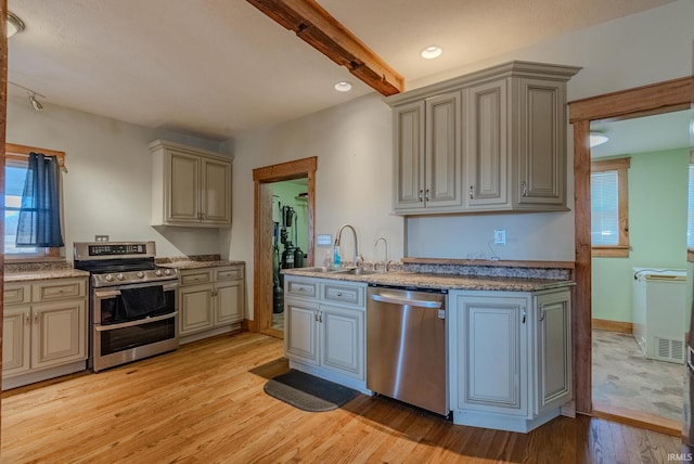 kitchen with appliances with stainless steel finishes, beam ceiling, light hardwood / wood-style floors, and sink