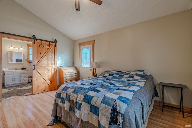 bedroom with connected bathroom, lofted ceiling, ceiling fan, a barn door, and light wood-type flooring