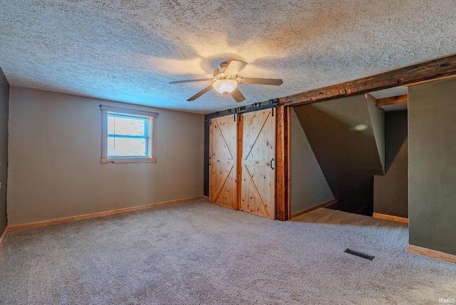 unfurnished bedroom with ceiling fan, a barn door, carpet floors, and a textured ceiling