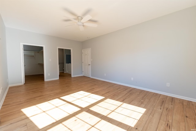 unfurnished bedroom with ceiling fan, a spacious closet, a closet, and light hardwood / wood-style flooring