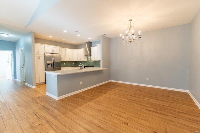 kitchen featuring pendant lighting, white cabinets, stainless steel fridge with ice dispenser, decorative backsplash, and wall chimney exhaust hood