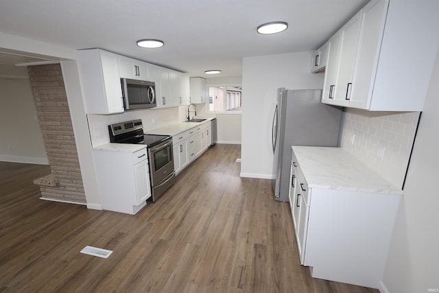 kitchen featuring appliances with stainless steel finishes, hardwood / wood-style floors, white cabinetry, sink, and light stone counters