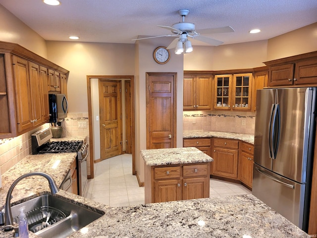 kitchen featuring light tile patterned flooring, sink, light stone counters, a center island, and stainless steel appliances