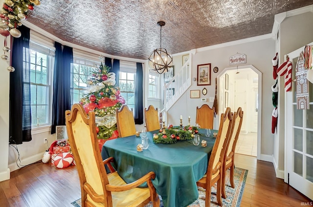 dining space with crown molding, wood-type flooring, a chandelier, and a healthy amount of sunlight