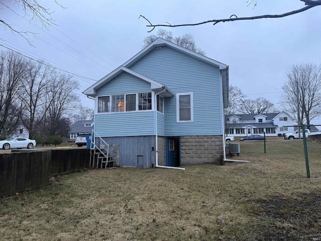 rear view of house with central AC unit and a lawn