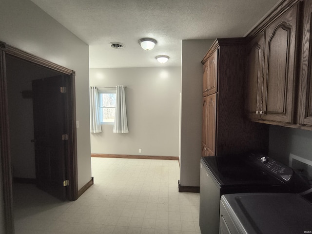 clothes washing area with a textured ceiling, cabinets, and washing machine and clothes dryer