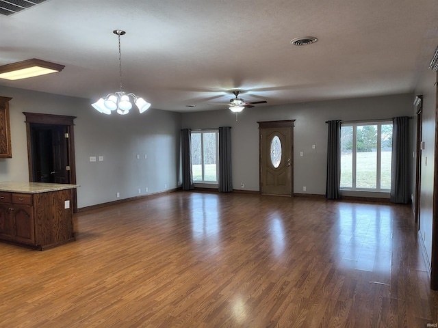 unfurnished living room with ceiling fan with notable chandelier, plenty of natural light, and hardwood / wood-style floors