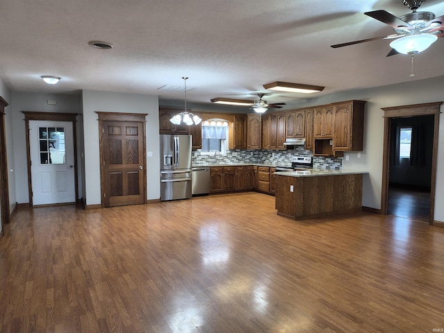 kitchen with appliances with stainless steel finishes, pendant lighting, decorative backsplash, and kitchen peninsula