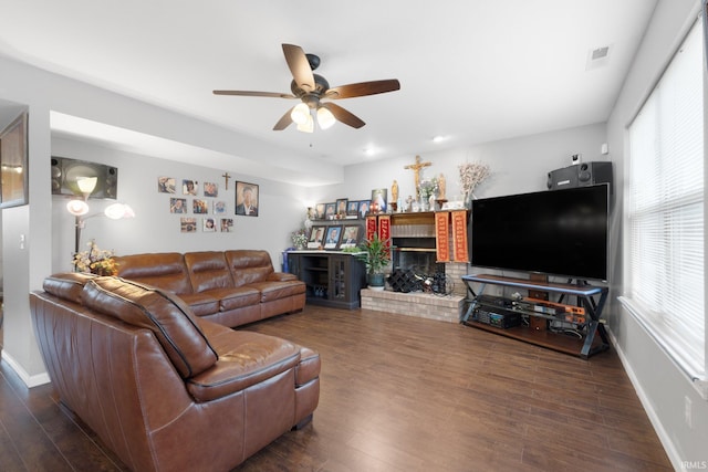 living room featuring dark wood-type flooring, ceiling fan, and a brick fireplace