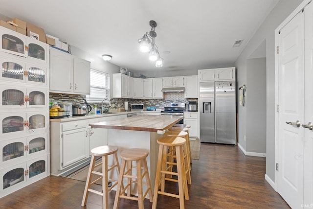 kitchen featuring appliances with stainless steel finishes, decorative light fixtures, white cabinetry, wooden counters, and a center island