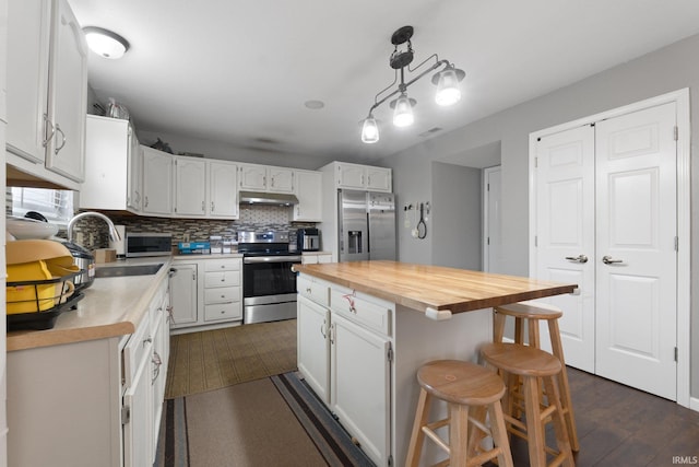 kitchen with a kitchen island, appliances with stainless steel finishes, white cabinetry, wooden counters, and backsplash