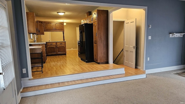 kitchen featuring sink, black refrigerator, and light colored carpet