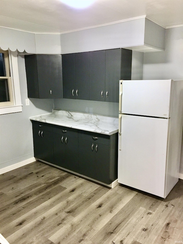 kitchen featuring white refrigerator, crown molding, light stone countertops, and light hardwood / wood-style flooring