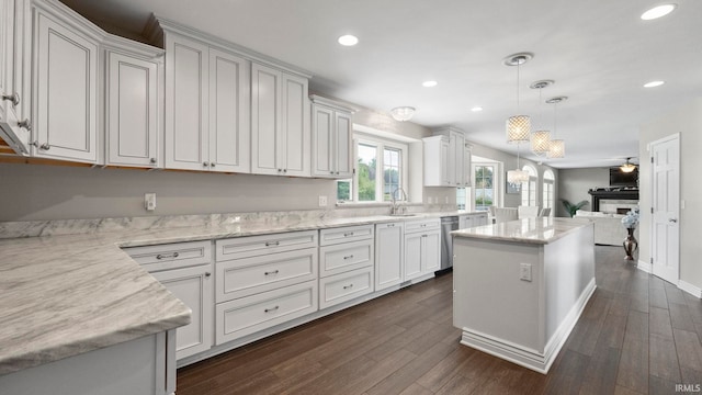 kitchen with pendant lighting, a center island, light stone counters, white cabinets, and stainless steel dishwasher