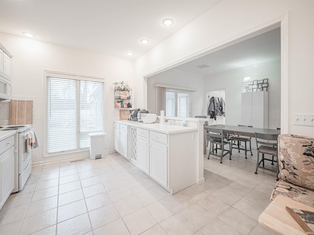 kitchen featuring light tile patterned floors, white appliances, kitchen peninsula, and white cabinets