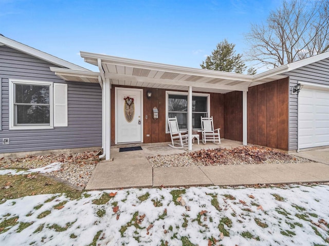 snow covered property entrance featuring a garage and covered porch