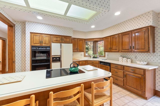 kitchen with a skylight, a kitchen bar, decorative backsplash, light tile patterned floors, and black appliances