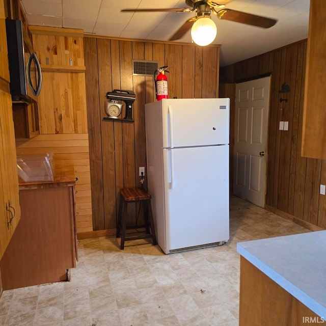 kitchen featuring white refrigerator, ceiling fan, and wood walls