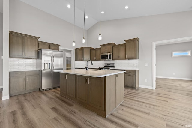 kitchen with sink, a center island with sink, light wood-type flooring, pendant lighting, and stainless steel appliances