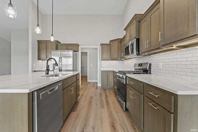 kitchen featuring sink, appliances with stainless steel finishes, light stone countertops, decorative light fixtures, and light wood-type flooring