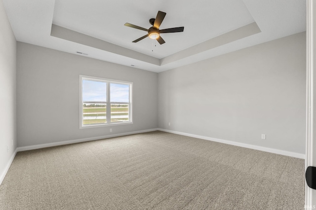 empty room featuring a raised ceiling, ceiling fan, and carpet