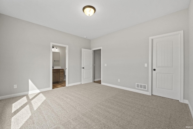 unfurnished bedroom featuring ensuite bath and carpet flooring