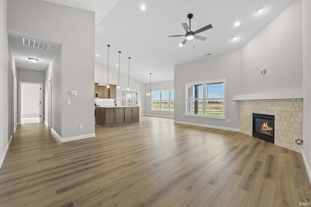 unfurnished living room featuring a tiled fireplace, hardwood / wood-style flooring, ceiling fan with notable chandelier, and high vaulted ceiling