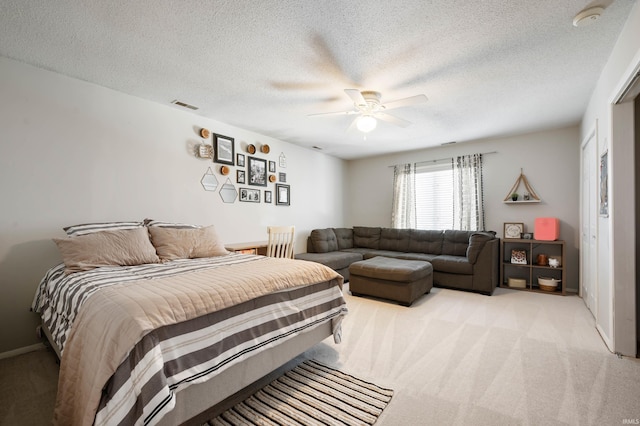 bedroom with ceiling fan, light carpet, and a textured ceiling