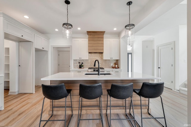 kitchen with tasteful backsplash, sink, an island with sink, and white cabinets