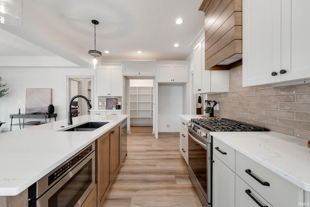 kitchen with pendant lighting, stainless steel appliances, white cabinets, and a center island with sink