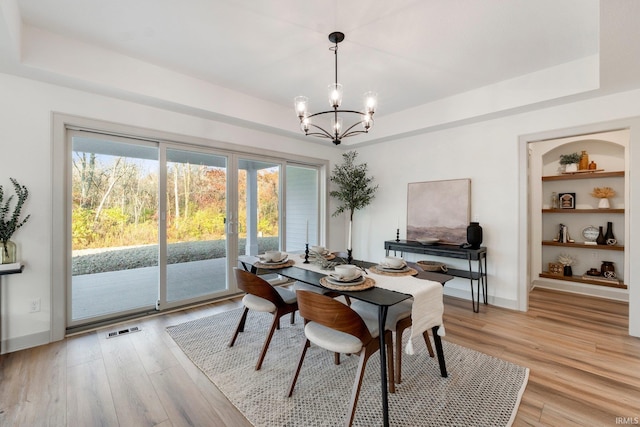 dining area with a chandelier, a raised ceiling, built in features, and light hardwood / wood-style flooring